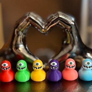 May include: Six colorful rubber duckies with a single large eye and a toothy grin. The duckies are arranged in a row from left to right: red, green, yellow, purple, pink, and blue.