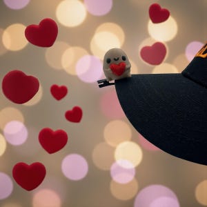 May include: A black baseball cap with a small, tan figurine holding a red heart. Red heart-shaped decorations float in the background. The figurine is attached to the brim of the cap.
