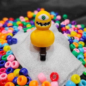 May include: Yellow monster hair clip with a single green eye and a toothy grin. The clip is surrounded by colorful beads.
