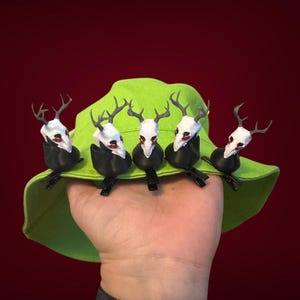 May include: A lime green bucket hat with five white deer skull clips attached to the brim. The deer skulls have black antlers and red eyes.