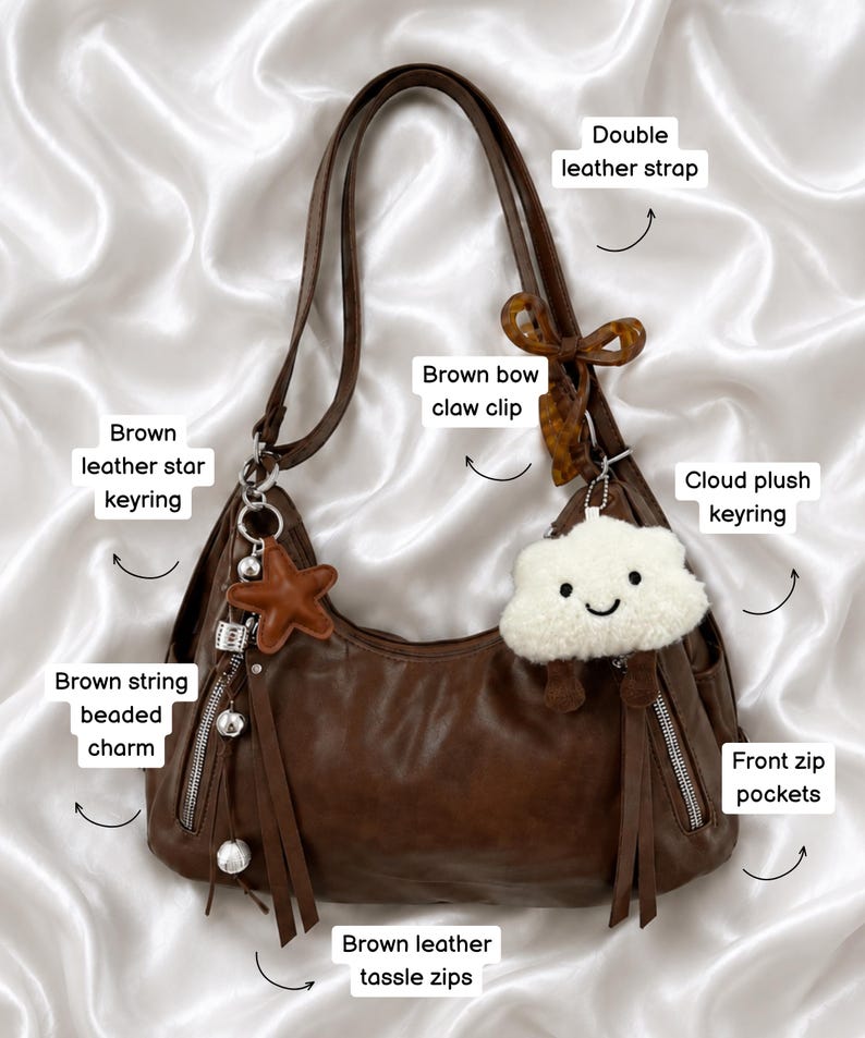 May include: A brown leather shoulder bag featuring double leather straps, front zip pockets with brown leather tassel pulls, and a brown string beaded charm. Accessories include a brown leather star keyring, a cloud plush keyring, and a brown bow claw clip.