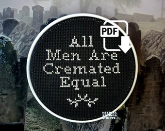 May include: A black and white cross-stitch embroidery hoop with the text "All Men Are Cremated Equal" and a skull and crossbones symbol. The hoop is in front of a blurry background of a graveyard.