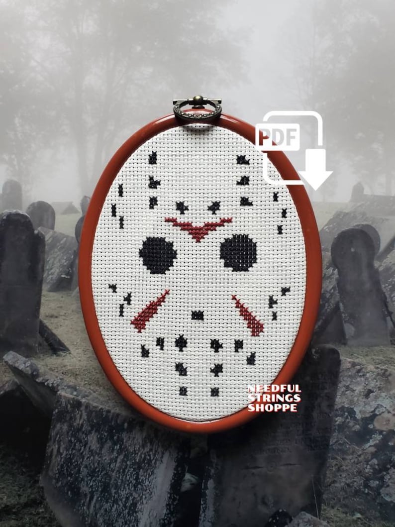 May include: A white cross-stitch pattern of a hockey mask in a red oval frame. The frame is hanging on a wall with a foggy background. The text "PDF" is in a white box with a downward arrow.