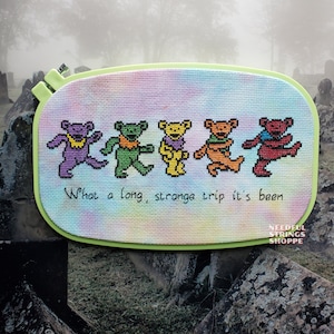 May include: A cross-stitch piece featuring five colorful dancing bears in purple, green, yellow, orange, and red. The text "What a long, strange trip it's been" is stitched below the bears. The piece is mounted in a light green hoop.