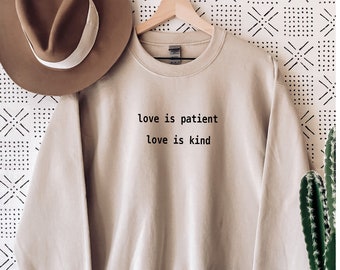 May include: A beige sweatshirt with the text "love is patient love is kind" printed on the front.