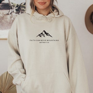May include: A cream colored hoodie with a black mountain graphic and the text "FAITH CAN MOVE MOUNTAINS" and "MATTHEW 17:20".