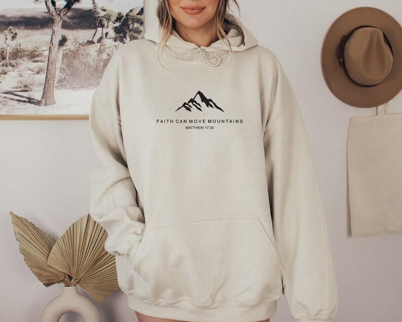 May include: A cream colored hoodie with a black mountain graphic and the text "FAITH CAN MOVE MOUNTAINS" and "MATTHEW 17:20".