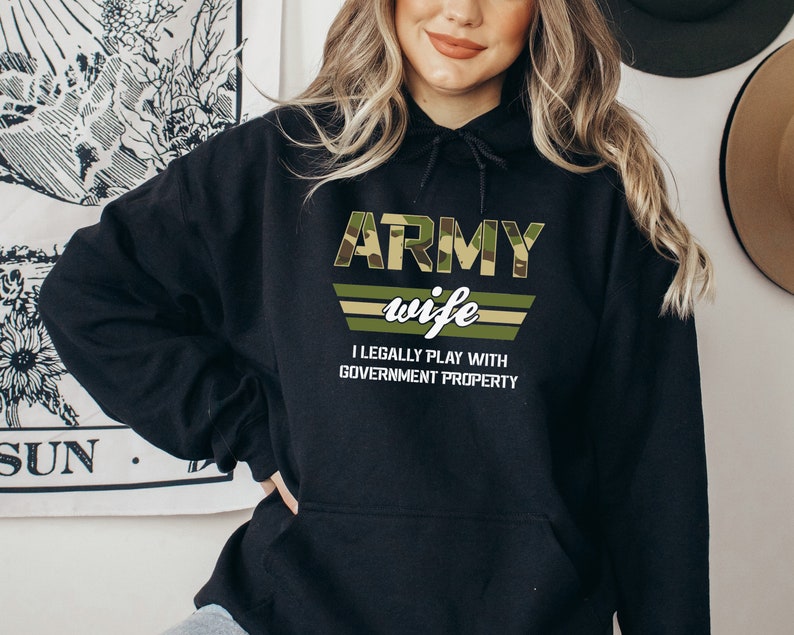May include: Black hooded sweatshirt with a camouflage print design that says "Army wife I legally play with government property".