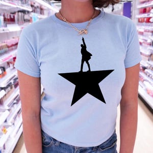 A person wearing a light blue t-shirt with a black silhouette of a person standing on a star.