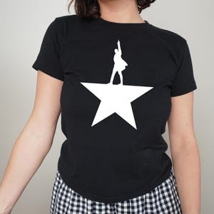 A person wearing a black t-shirt with a white star graphic and a silhouette of a person standing on a raised star.