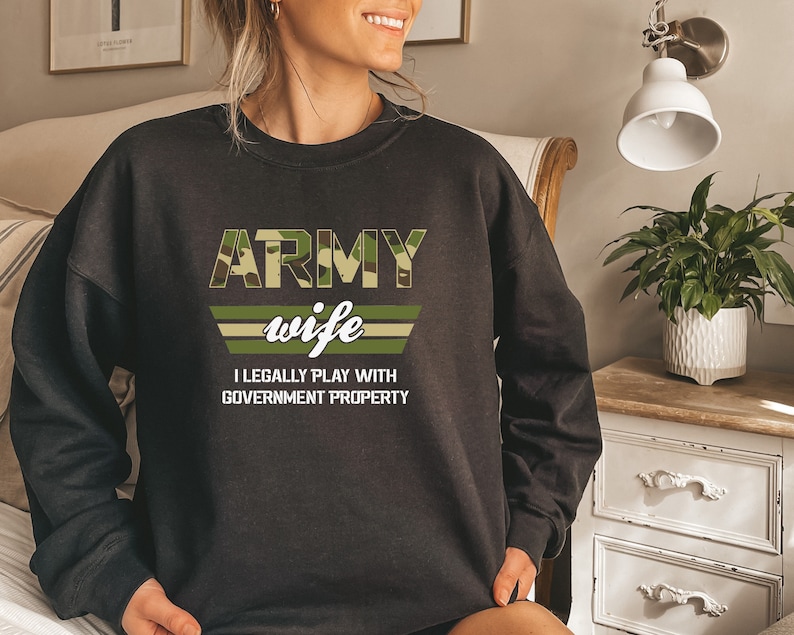May include: Black sweatshirt with a camouflage print and the text "ARMY wife I LEGALLY PLAY WITH GOVERNMENT PROPERTY".