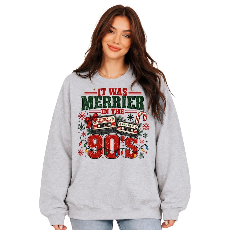 A woman wearing a gray sweatshirt with a graphic design featuring Christmas-themed elements and text.