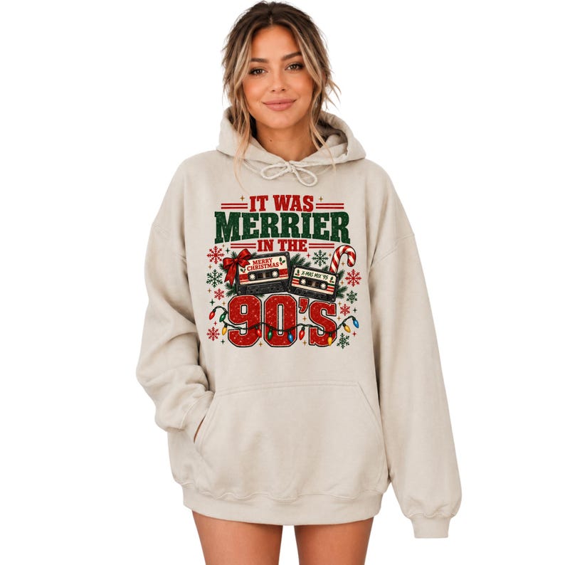 A woman wearing a beige hoodie with a graphic design featuring Christmas-themed elements and text.