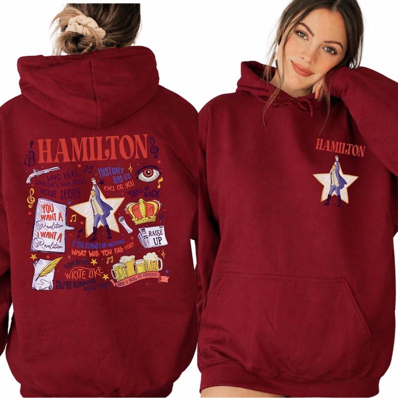 A red hoodie with various text and graphics printed on it, including the word "HAMILTON" and a star. The woman is posing with the hoodie on.
