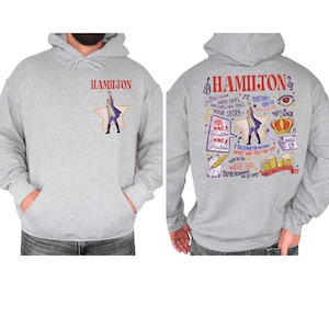 A gray hoodie with a colorful graphic design featuring various text elements and illustrations related to the character Hamilton from the musical Hamilton.