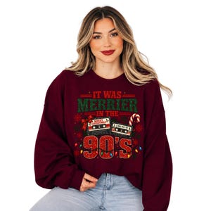 A woman wearing a burgundy sweater with a Christmas-themed design and text.