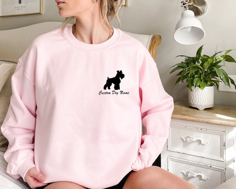 May include: A pink sweatshirt with a black silhouette of a Schnauzer dog and the text "Custom Dog Name".