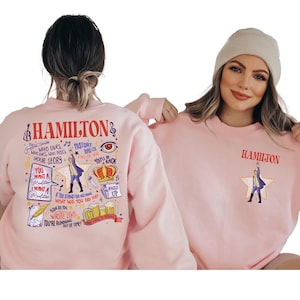 two women wearing pink sweatshirts with various text and illustrations related to the musical Hamilton.