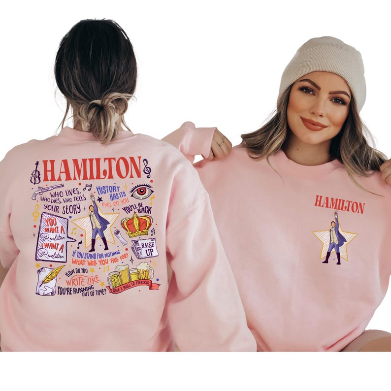 two women wearing pink sweatshirts with various text and illustrations related to the musical Hamilton.
