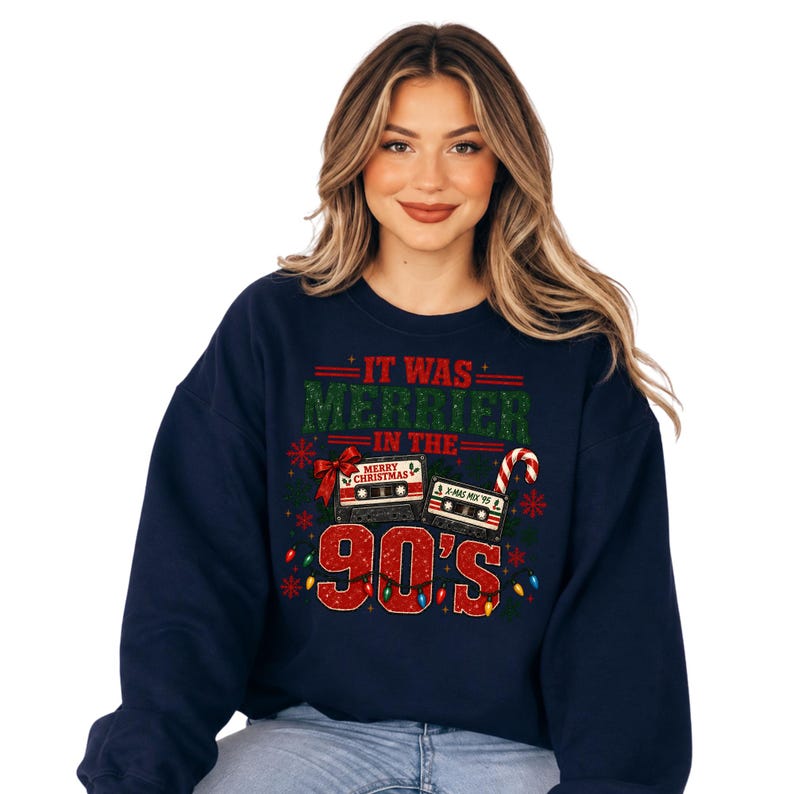 A woman wearing a navy blue sweatshirt with a graphic design featuring a Christmas tree, a cassette tape, and the text "It was merrier in the 90's".