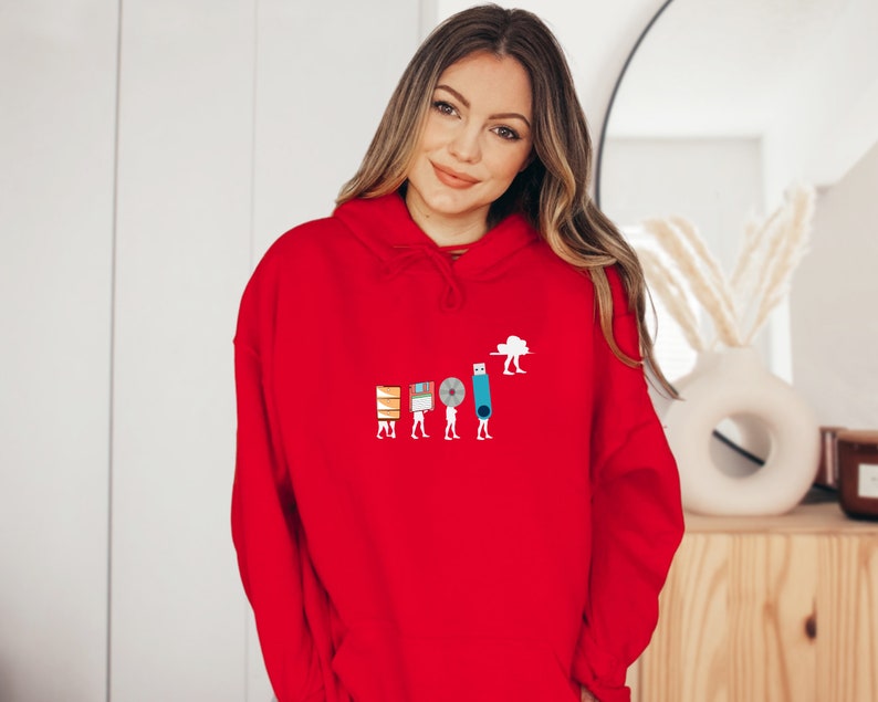 May include: A red hoodie with a graphic of a line of people carrying different types of storage devices, including a floppy disk, a CD, a USB drive, and a cloud. The graphic is in the center of the hoodie.
