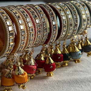 Peut inclure: Un ensemble de bracelets colorés avec des glands pendants. Les bracelets sont décorés de petits strass et de perles clairs. Les glands sont en fil de soie et se déclinent en plusieurs couleurs, notamment le rouge, le vert, le bleu et le jaune.