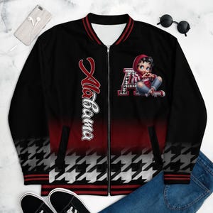 May include: Black and red bomber jacket with a white and black houndstooth pattern. The jacket has a zipper closure and features a cartoon character wearing a red hat and holding a heart. The text "Alabama" is printed on the left side of the jacket.