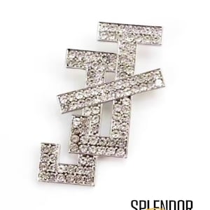May include: Silver-toned brooch in the shape of the letters J and T, encrusted with sparkling rhinestones. The brooch has a geometric design and is set against a white background. The word "SPLENDOR" and the word "Bling" are printed in black and gold.