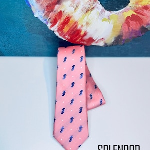 May include: A pink necktie with a repeating pattern of dark blue pixelated letter "F" shapes and small white dots. The tie is displayed against a white background with a colorful abstract painting in the background. The words "SPLENDOR BLING" are in the bottom right corner.