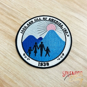 May include: Embroidered patch with the text "JACK AND JILL OF AMERICA, INC." in a circular design. The patch features a family silhouette in front of blue mountains, a pink sun, and the year "1938". The patch has a white border.