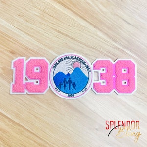 May include: Pink and white felt patch with the numbers 1938 and a logo that says "Jack and Jill of America, Inc. Est. 1938" with a sun, mountains, and a family of five.