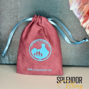 May include: A red velvet drawstring bag with a blue logo that says "Jack and Jill of America, Inc." and features a family of four standing on a mountain with a sun behind them. The logo also includes the year "1938". The bag has the website "www.splendorbling.com" printed on the bottom.