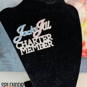 May include: A silver-toned pin with blue and pink rhinestones spelling out "Jack & Jill Charter Member".