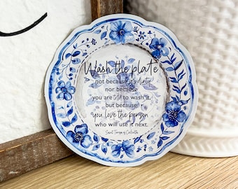 Op de afbeelding: Een bord met een blauw-wit bloemenpatroon met een citaat van Moeder Teresa dat luidt: "Was de schotel niet omdat hij vies is, noch omdat je dat moet doen, maar omdat je de persoon liefhebt die hem als volgende zal gebruiken."