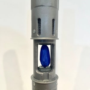 K&ouml;nnte beinhalten: Nahaufnahme eines grauen Metallger&auml;ts mit einem blauen Kristall im Inneren. Das Ger&auml;t hat eine Reihe kleiner L&ouml;cher oben und ein Etikett mit dem Text: "Dieses Ger&auml;t darf keine sch&auml;dlichen St&ouml;rungen verursachen..."