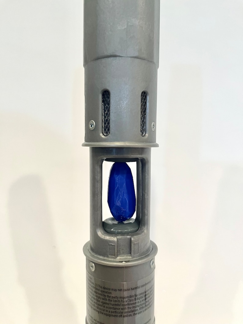 K&ouml;nnte beinhalten: Nahaufnahme eines grauen Metallger&auml;ts mit einem blauen Kristall im Inneren. Das Ger&auml;t hat eine Reihe kleiner L&ouml;cher oben und ein Etikett mit dem Text: "Dieses Ger&auml;t darf keine sch&auml;dlichen St&ouml;rungen verursachen..."