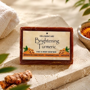 May include: A rectangular dark orange soap bar labeled Era Skincare Brightening Turmeric Face & Body Soap Bar. The label features illustrations of turmeric roots and text stating it brightens dark spots, is fragrance free, and anti acne.