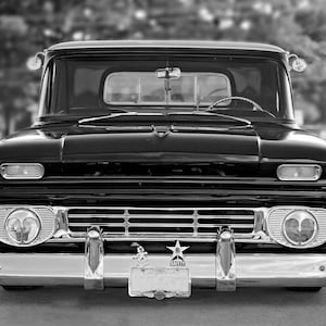 May include: Black and white photo of a classic black pickup truck with chrome accents. The truck is parked in front of a gas station.