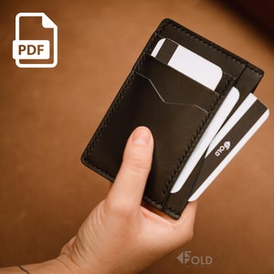 May include: A black leather card holder with a stitched edge, holding multiple cards. The cards have a white background with black stripes and the word "fold" printed on them.