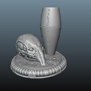 以下が含まれることがあります： 円形の台座の上に、エイリアンの頭蓋骨の3Dプリントモデルが置かれ、その上に円柱形のオブジェクトが直立している。円柱には表面に文字が刻まれている。グレーのモデルです。