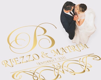 May include: A gold wedding ceremony floor decal with a large letter "B" and the text "RITEZZO & MATRIM" and "NOVEMBER 7, 2021". A bride and groom are standing on the decal, looking at each other.