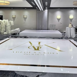 May include: A large, white dance floor with gold trim and gold lettering that reads "AK" and "ADEOLA & KOFI #KWIK24". The room has tables with white tablecloths and gold chairs, and a stage.
