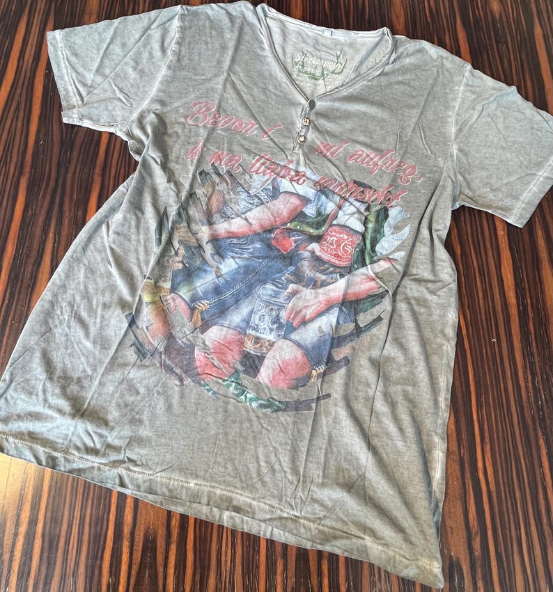 May include: A light green short-sleeve shirt with a V-neck and button closure. The shirt features a graphic print of a man with a beer stein and text that reads "Beyond all limits".