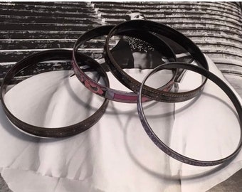 May include: Four black bangle bracelets with a floral design. The bracelets have a pink, white, and black pattern.