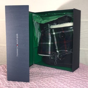 Puede incluir: Un par de botas de invierno negras con un patr&oacute;n de cuadros y un forro de piel blanca, dentro de una caja azul con el logotipo de Tommy Hilfiger.