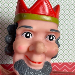 Peut inclure: Une tête de marionnette rouge et verte avec une couronne, une barbe grise et un visage souriant.