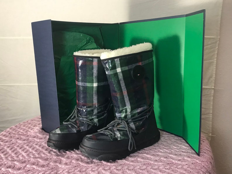 Puede incluir: Un par de botas de invierno negras y verdes a cuadros con forro de piel blanca y un detalle de bot&oacute;n negro. Las botas est&aacute;n en una caja con forro verde.