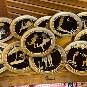 Puede incluir: Conjunto de diez posavasos redondos con diseños en negro y dorado. Cada posavasos presenta una ilustración diferente de una pareja en un estilo juguetón y caprichoso.