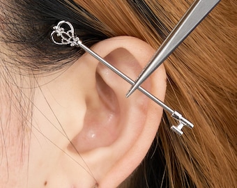 May include: Silver industrial barbell earring with a key design at one end and a keyhole design at the other. A pair of silver hoop earrings are also visible. The word "JEWSEN" is at the bottom of the image.