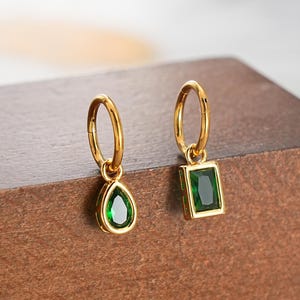 May include: A pair of gold-colored hoop earrings, one with a teardrop-shaped green gemstone and the other with a rectangular green gemstone. The word "JEWSEEN" is printed at the bottom of the image.
